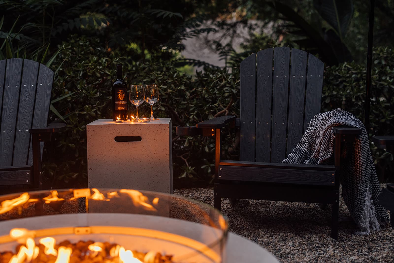 The garden fire pit at dusk, chairs pulled around it and a hammock beyond