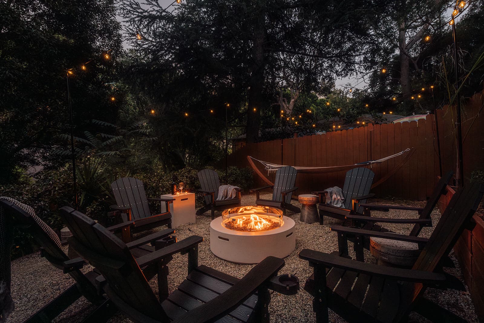 The fire pit and a circle of chairs under string lights after dark