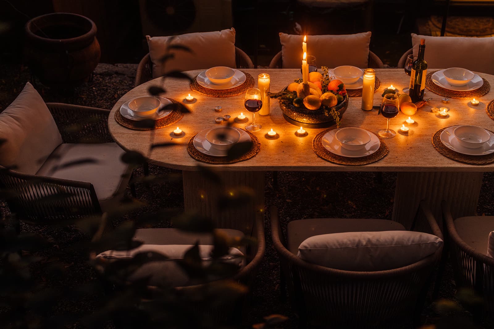 A candlelit table set for dinner outdoors, citrus at its center
